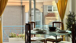 Un comedor con una mesa de vidrio y sillas, vista a un edificio y cortinas amarillas.