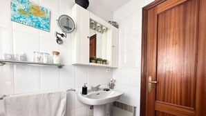 Un baño con puerta de madera, azulejos blancos, un lavabo, un espejo, un perchero para toallas y un taburete pequeño de madera.