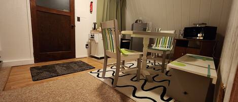 Una cocina compacta con puerta de madera, un refrigerador pequeño, un microondas y una mesa de comedor con sillas.