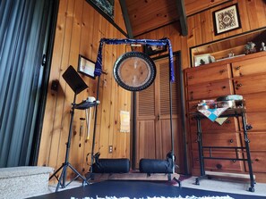 A room with wooden walls, a black drum, a drum stand, a black bag, a small table with dishes, and a wooden cabinet.