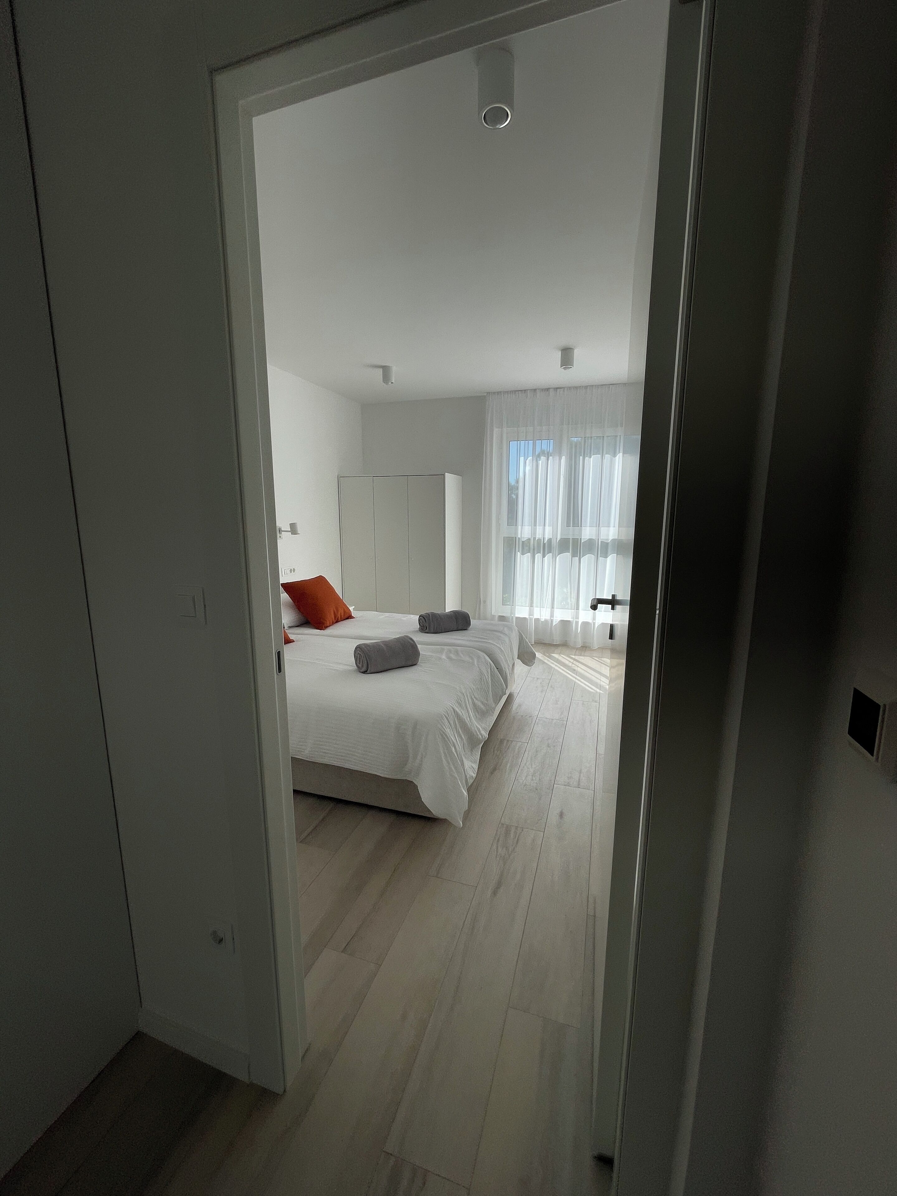 A modern bedroom with a large bed, a wardrobe, and a window with sheer curtains.
