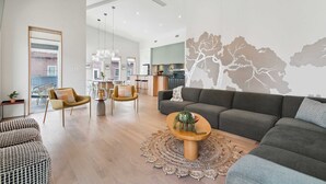 A modern living room with a grey sofa, a round coffee table with plants, a patterned rug, and a dining area with chairs and a table. - NOLA | Heated Pool | Private Hot Tub (New Orleans)