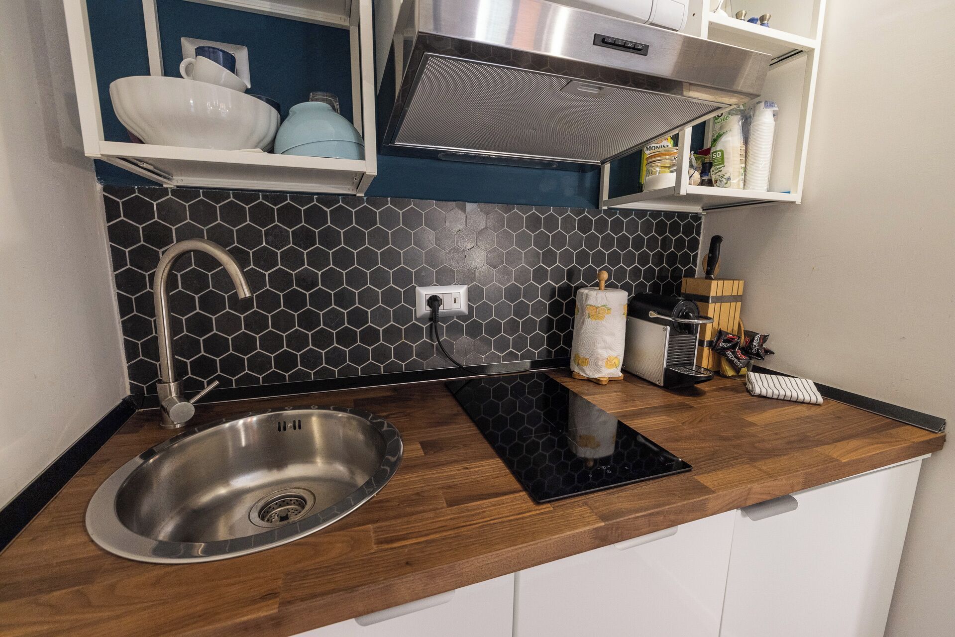 A modern kitchen with a stainless steel sink, a black hexagonal backsplash, and wooden countertops.