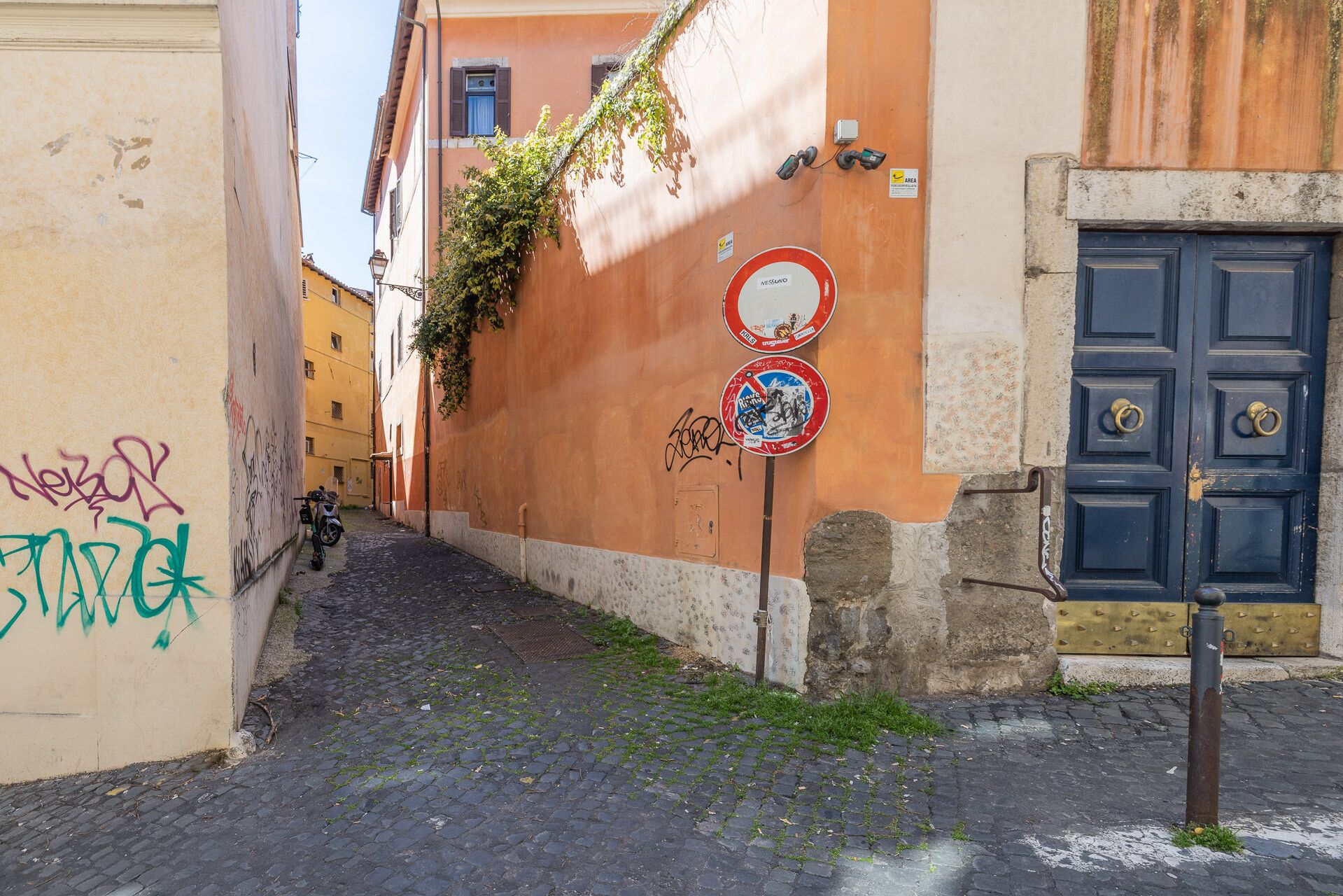 Une ruelle étroite pavée, avec un bâtiment dont la porte est bleue et dont le mur est couvert de graffitis.