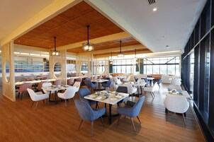Un restaurante espacioso con piso de madera, sillas modernas y amplios ventanales que dejan entrar la luz natural.