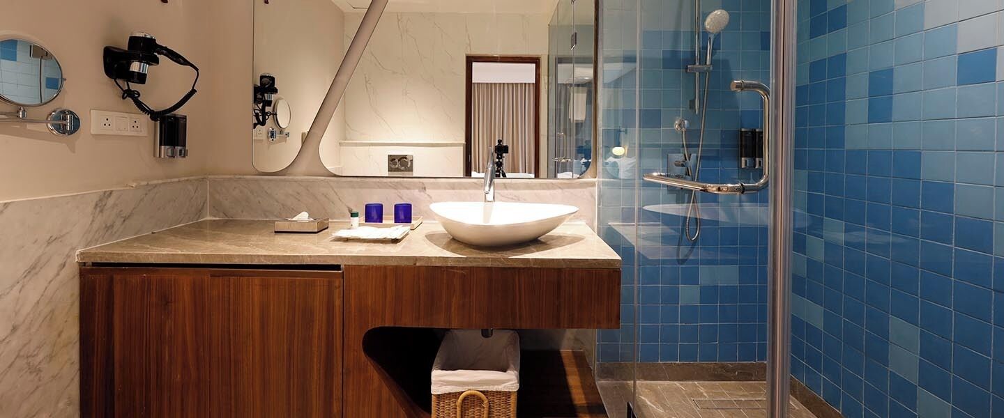 Ein Badezimmer mit einem großen Spiegel, einem weißen Waschbecken, einer hölzernen Waschtischunterschrank und einer Duschkabine mit blauen Fliesen.