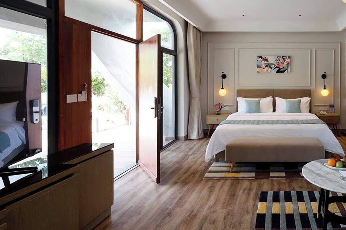 Una habitación de hotel moderna con una cama grande, un sofá, un televisor y una mesa de comedor con fruta.