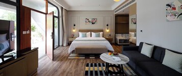 Una habitación de hotel moderna con una cama grande, un sofá, un televisor y una mesa de comedor con fruta.