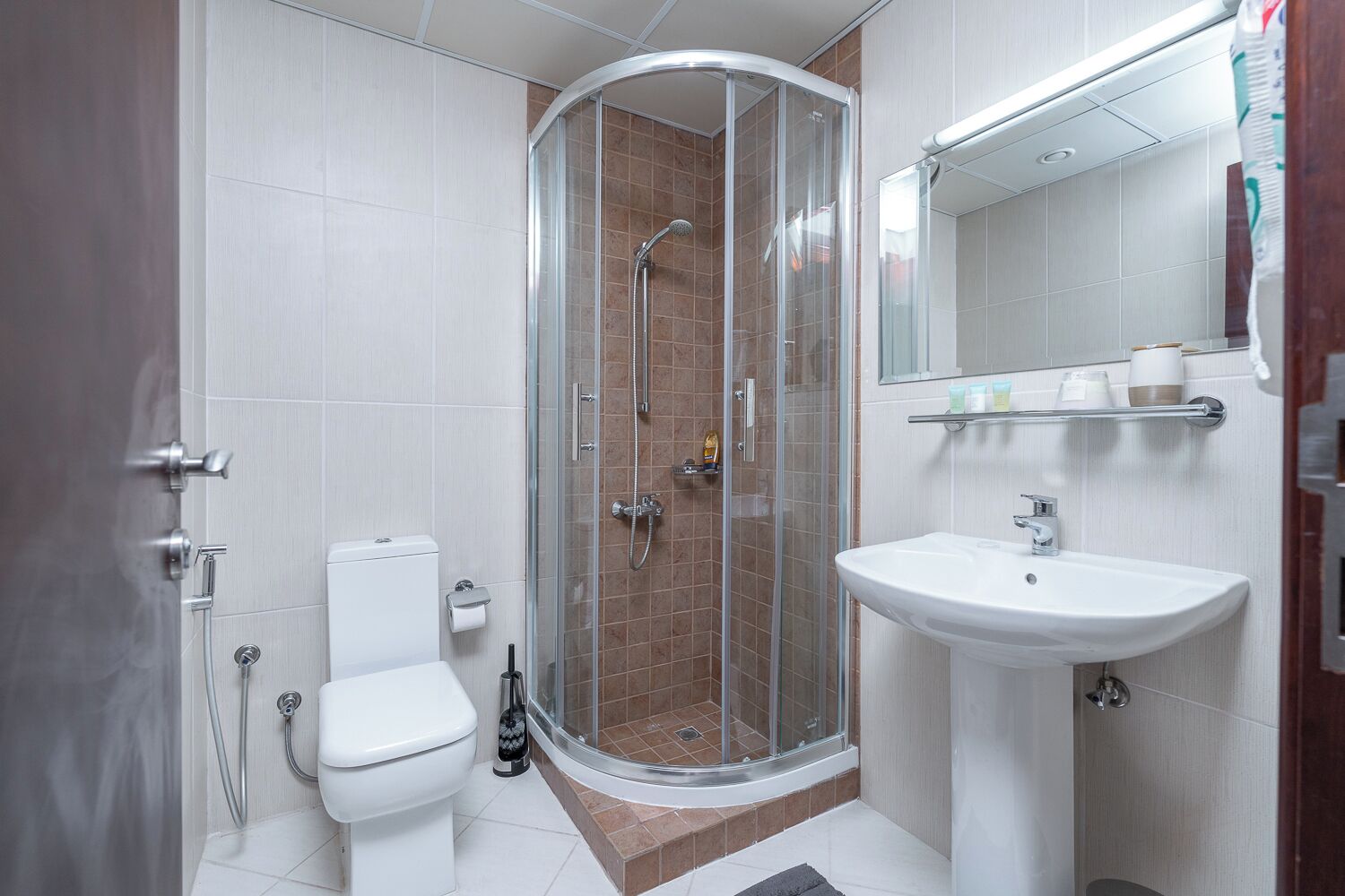 Un bagno moderno con cabina doccia in vetro, un water bianco e un lavabo con specchio soprastante.
