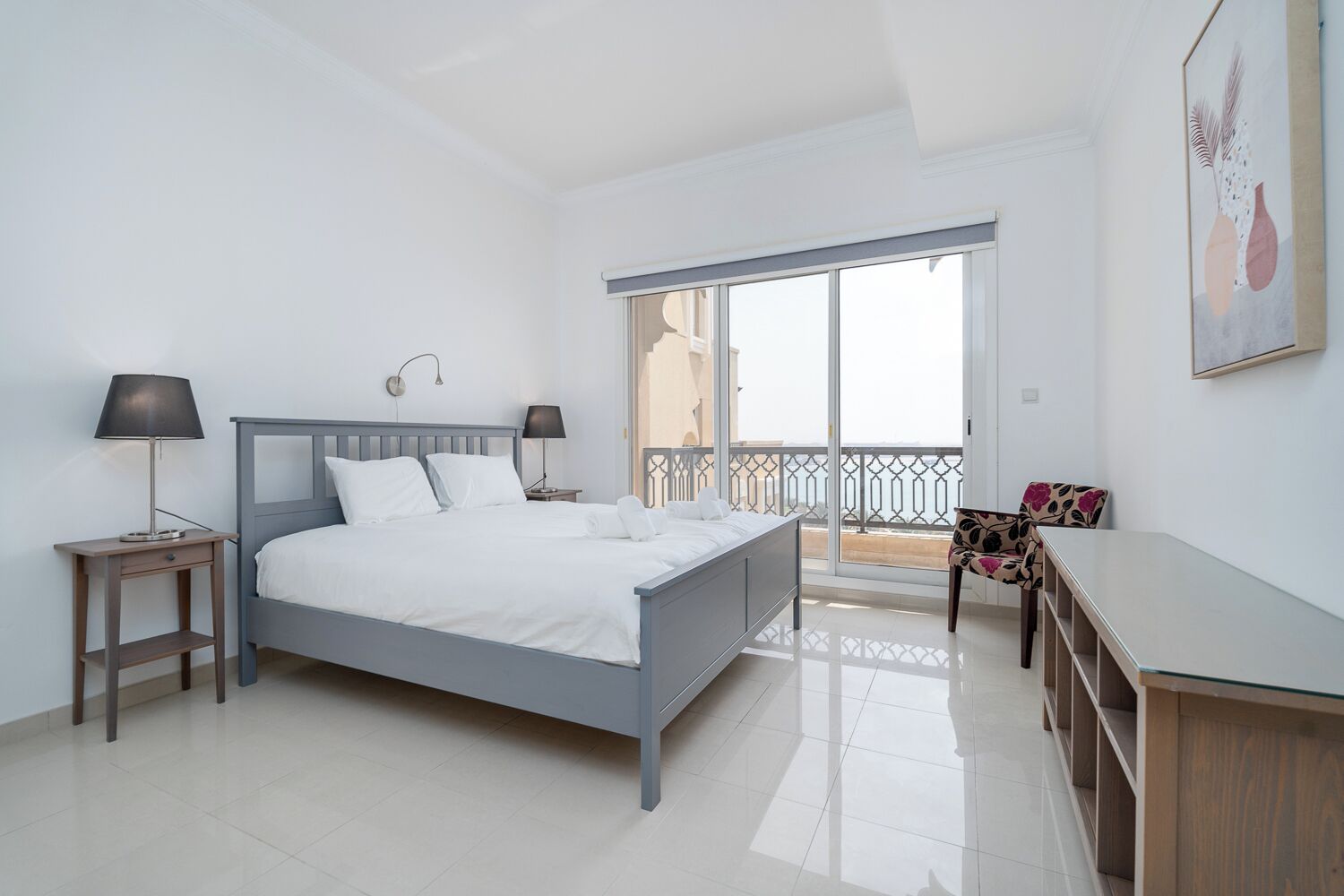 Un dormitorio moderno con cama, mesitas de noche, una silla y un balcón con barandilla.