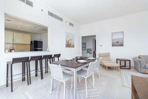 Una sala de estar moderna con comedor, un sofá y una cocina visible a través de un ventanal.