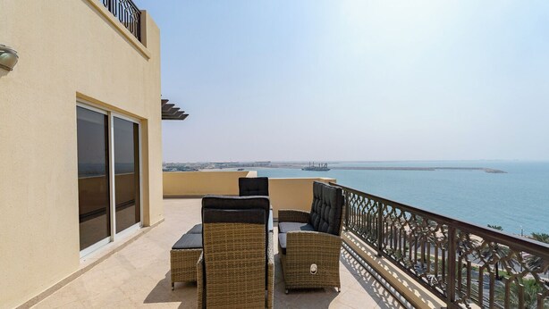 A balcony with wicker furniture, a sliding glass door, and a view of the sea. - Czechin - Kahraman Building (Ras Al Khaimah)