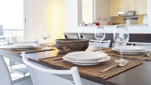 A dining table set with plates, glasses, and a decorative bowl, with a kitchen in the background. - Czechin - Kahraman Building (Ras Al Khaimah)