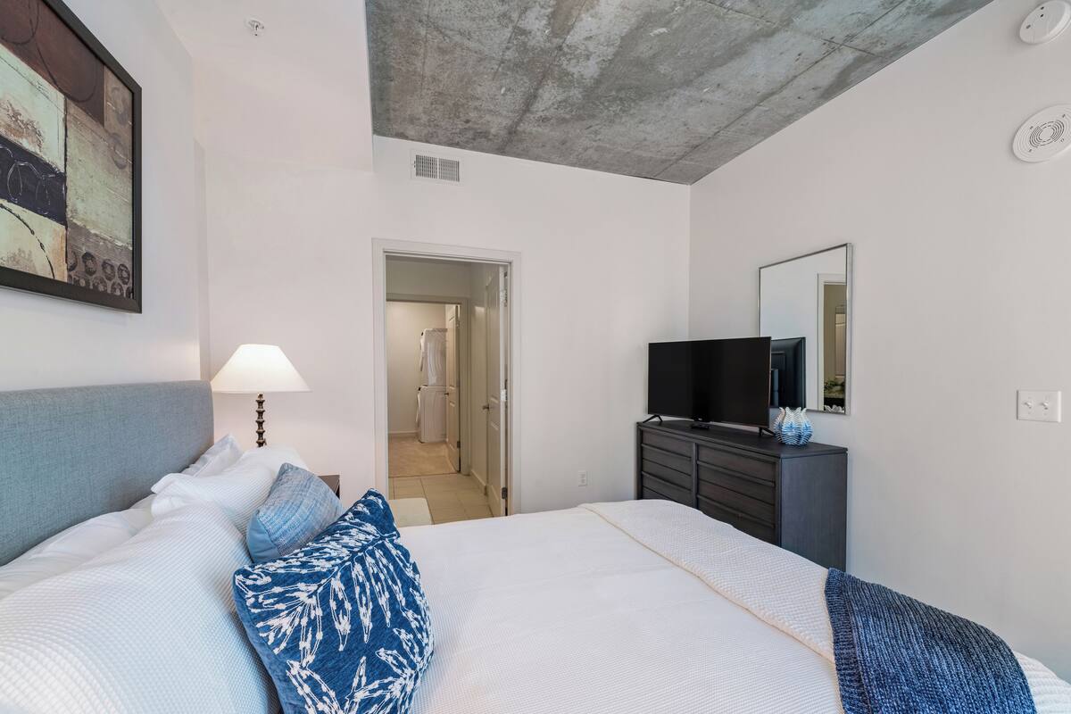 Une chambre à coucher avec un lit, une commode, un téléviseur et un tableau accroché au mur.