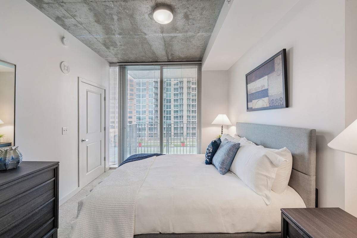 Une chambre moderne avec un grand lit, une commode, une table de chevet et une fenêtre donnant sur la ville.