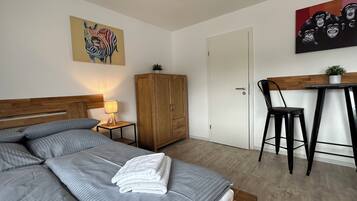 Een keurig opgeruimde slaapkamer met een bed, een houten garderobe, een bureau met stoel en twee schilderijen aan de muur.