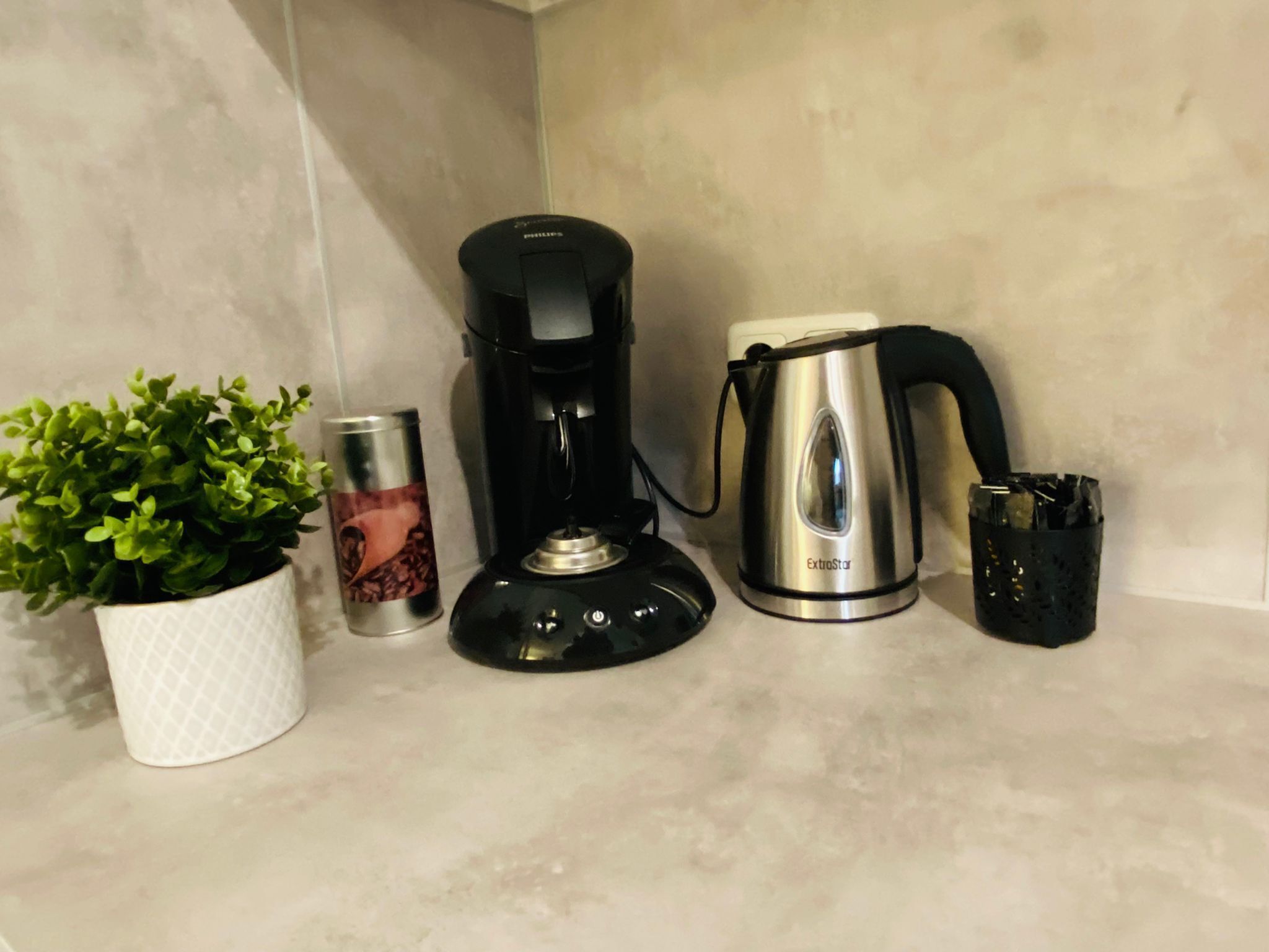 Eine Küchenarbeitsplatte mit Kaffeemaschine, Wasserkocher, Pflanze und einer Vorratsdose.