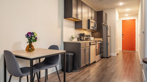 A modern kitchen with dark cabinets, a microwave, and a refrigerator. There is a dining table with chairs and a vase of flowers.