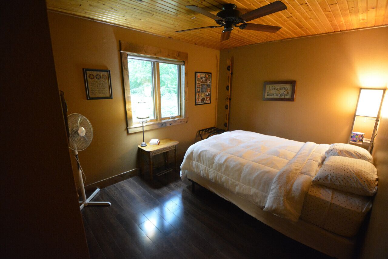 A bedroom with a bed, a standing fan, a window, and a ceiling fan.