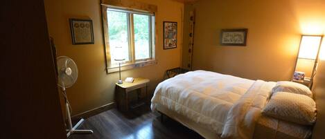 A bedroom with a bed, a standing fan, a window, and a ceiling fan.