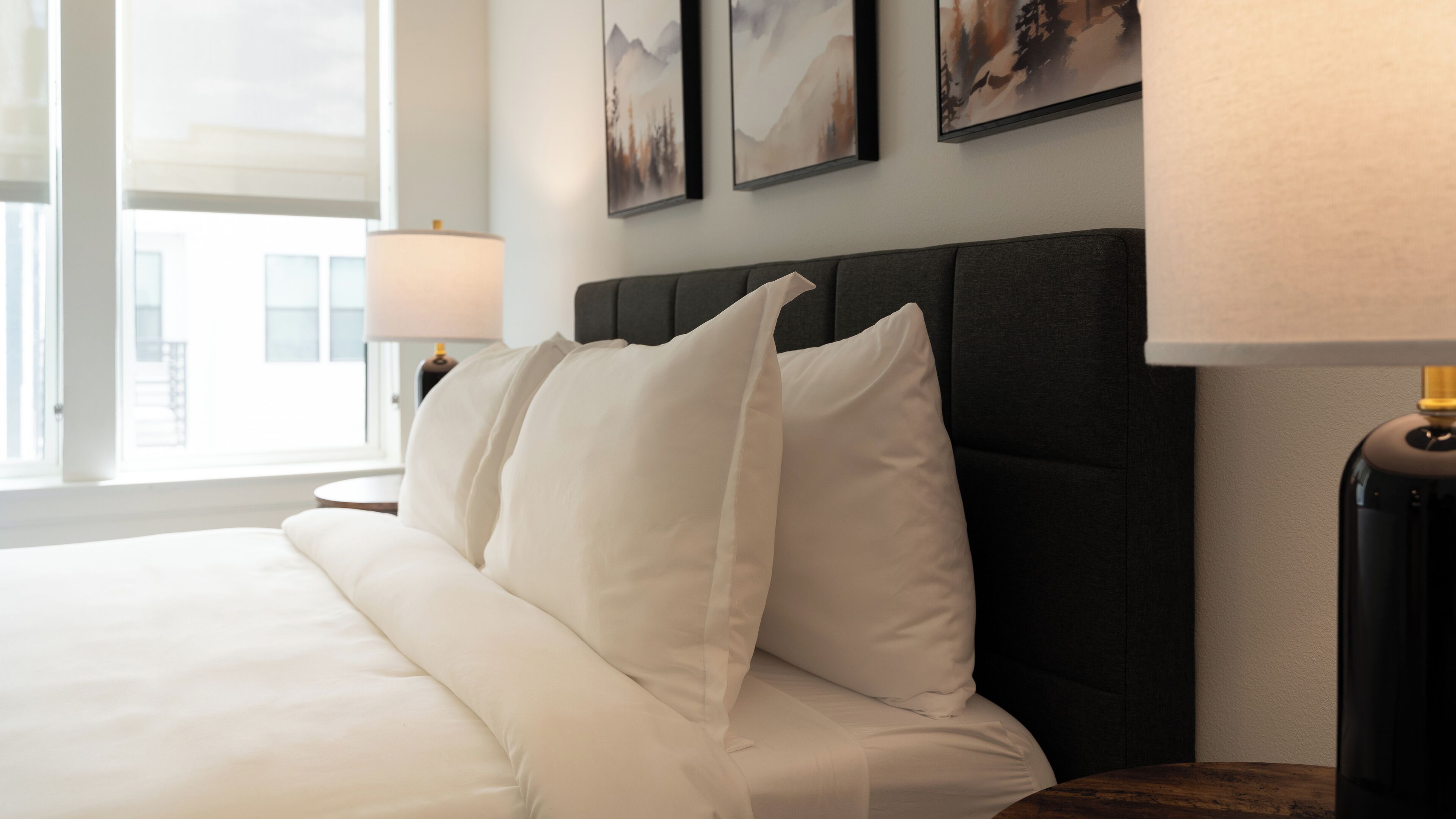 A neatly made bed with white linens, a dark headboard, and a bedside lamp.