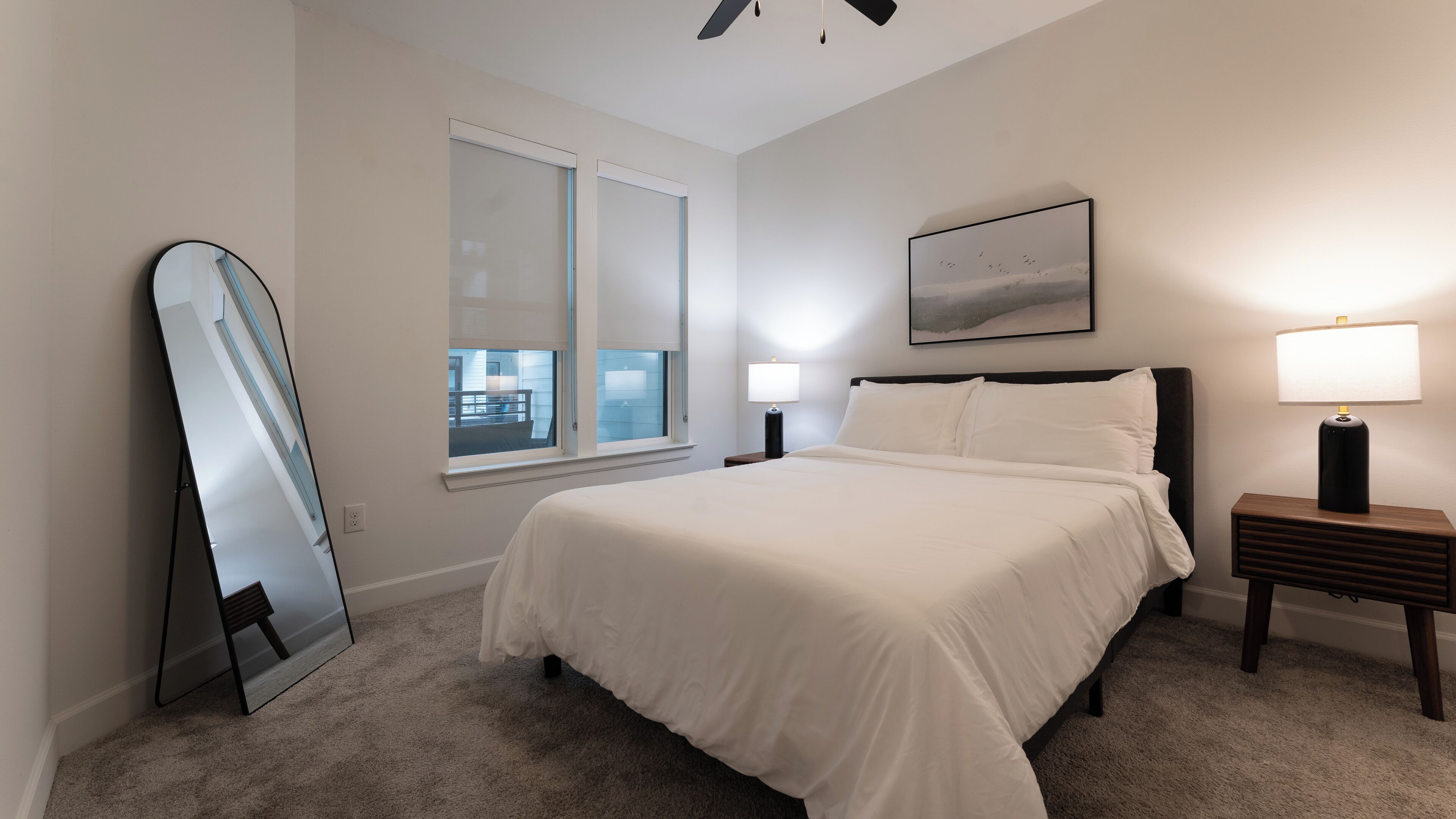 A bedroom with a bed, a nightstand, a lamp, a window, and a painting on the wall.