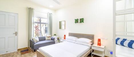 A hotel room with a bed, a desk, a chair, a ceiling fan, a window with curtains, and a door.