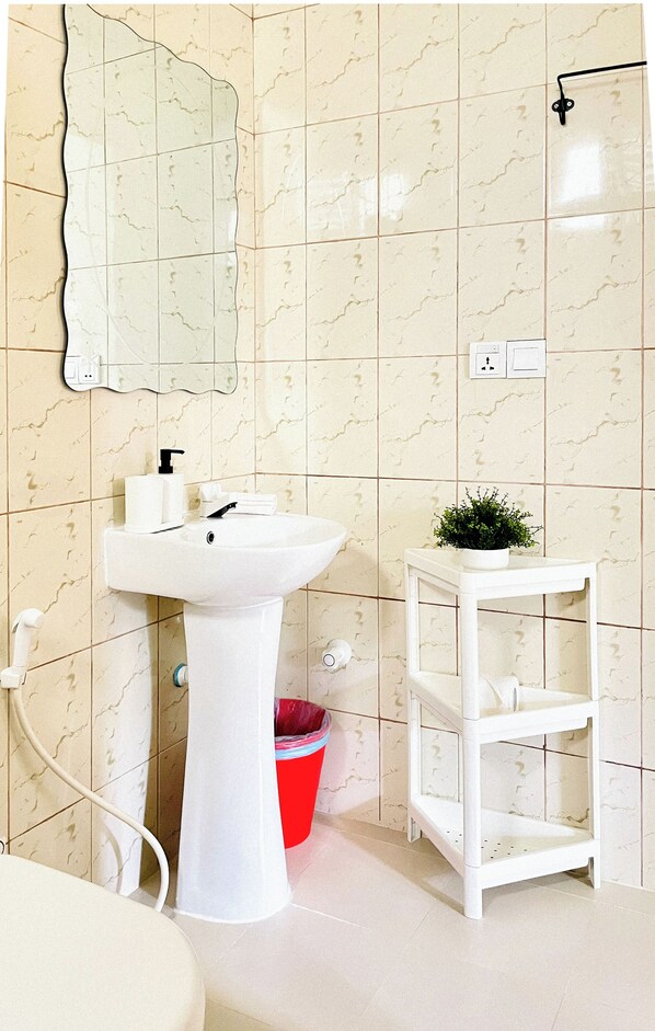 A bathroom with a white sink, a mirror, a red trash bin, and a white shelf. - Three Hearts Guesthouse (Fulhadhoo)