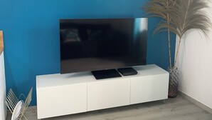 A room with a blue accent wall, a flat-screen TV mounted on a white cabinet, a tall potted plant, and a small table with a chair.