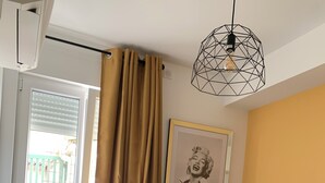 A bedroom with a bed, a standing lamp, a framed picture on the wall, and a window with curtains.