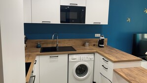 A compact kitchen with white cabinets, a black microwave, a sink, a coffee maker, and a washing machine.