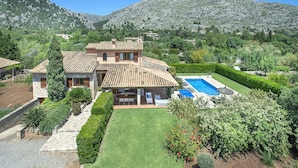 Une grande maison avec une piscine, entourée de jardins bien entretenus et dominée par un paysage montagneux.