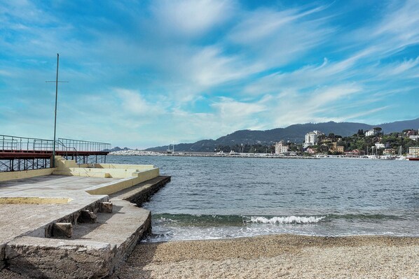 A coastal promenade with a concrete walkway, a metal railing, and a pebble beach. - Sea View Flat in Rapallo by Wonderful Italy (Rapallo)