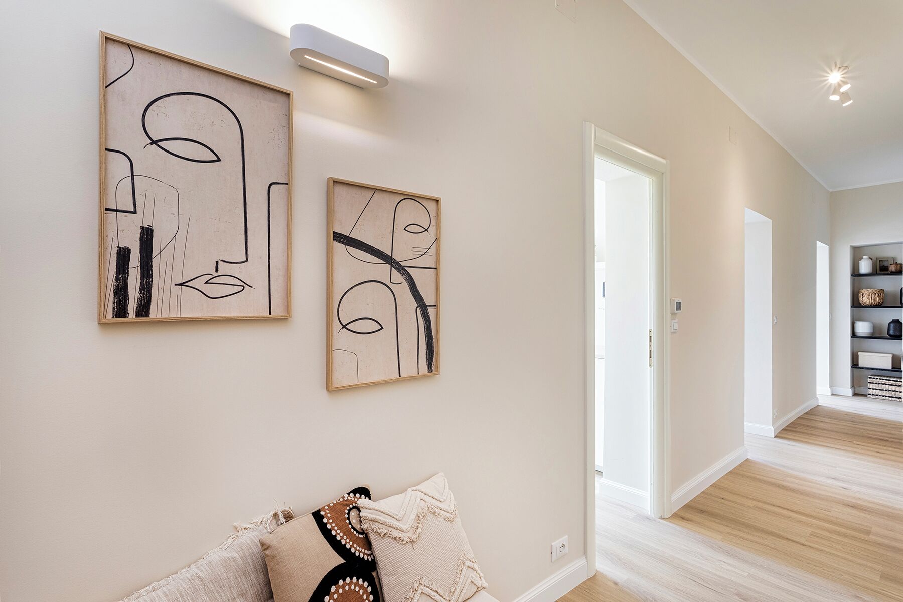 Un intérieur moderne agrémenté d’œuvres d’art abstraites sur les murs, un couloir menant à une salle à manger et une étagère de cuisine bien visible.