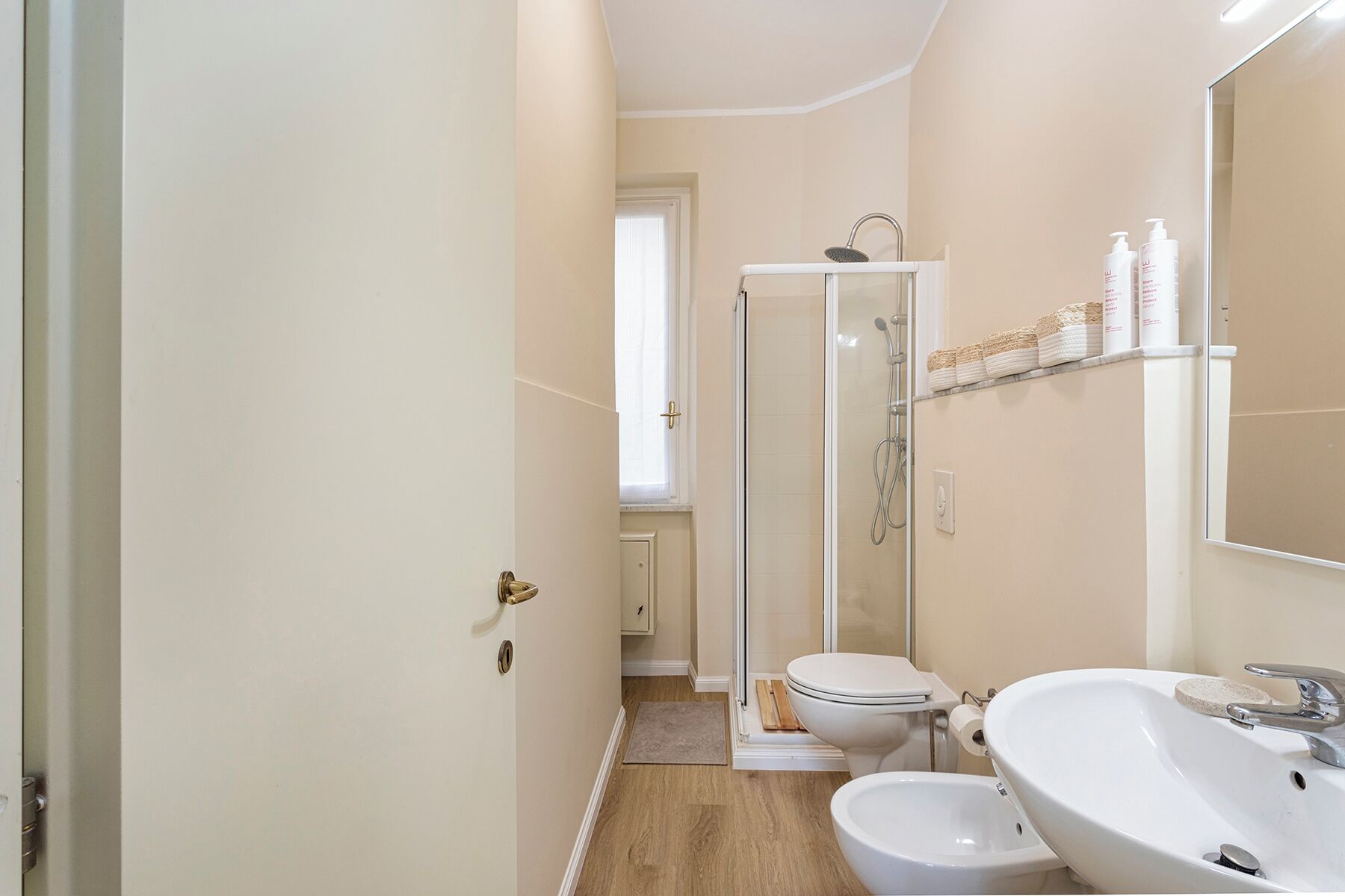 A bathroom with a shower, toilet, bidet, sink, and a mirror.