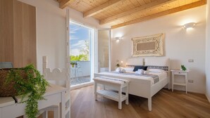 A bedroom with a wooden ceiling, a bed with a patterned headboard, a bedside table, a bench, and a view of the outdoors. - ClickSardegna Villa Celeste: Countryside Deluxe near the beaches of Sardinia (Alghero)