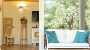 A room with a wooden ceiling, a white sofa with blue cushions, and a large window with a view of trees. - ClickSardegna Villa Celeste: Countryside Deluxe near the beaches of Sardinia (Alghero)