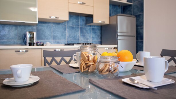 A modern kitchen with blue tiles, a dining table with placemats, and jars of cookies and nuts. - Souvenir 7 - Two Bedroom Apartment, Sleeps 6 (Gabicce Mare)