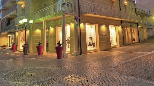 Hotel de vários andares com varandas, área de entrada pavimentada e plantas em vasos.