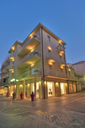 Hotel de vários andares com varandas, área de entrada pavimentada e plantas em vasos.
