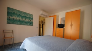 Quarto com cama, poltrona, aparelho de ar condicionado, guarda-roupa e televisão.