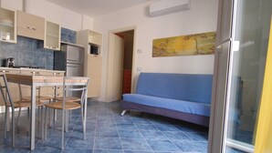 Um espaço de estar compacto com cozinha compacta, área de refeições com cadeiras, sofá e uma janela grande.