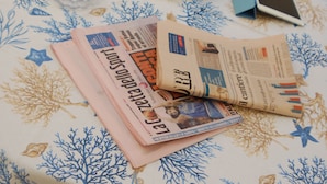 Jornais sobre uma mesa com toalha de mesa estampada com padrão de coral.
