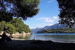 A lakeside scene with a person sitting on a bench and another person standing by the water. - Luxury Villa with Pool overlooking a Majestic View (J584+62 Archaia Epidauros)