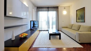Ein modernes Wohnzimmer mit einer Couch, einem Couchtisch, einem Fernseher auf einem Schrank und einer Obstschale auf der Arbeitsplatte.