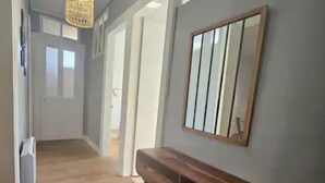 A hallway with wooden flooring, a bench, a hanging light fixture, and a mirror on the wall. - Le Galliéni Hyper Centre  (Le havre)