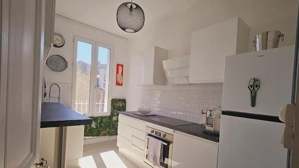 A modern kitchen with white cabinets, a black countertop, and a built-in oven. There is a window with a view of the outside, and a hanging light fixture above the counter. - Le Galliéni Hyper Centre  (Le havre)