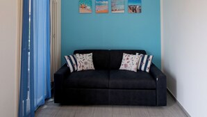 Quarto com sofá preto, paredes azuis e luminária de teto amarela.