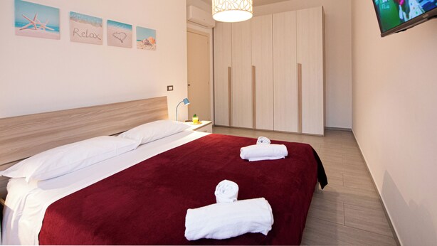 Quarto de hotel com uma cama grande, televisão na parede e um guarda-roupa.
