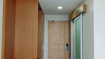 Un pasillo con un armario de madera, un escritorio con una botella de agua y una taza, y una puerta con un panel verde.